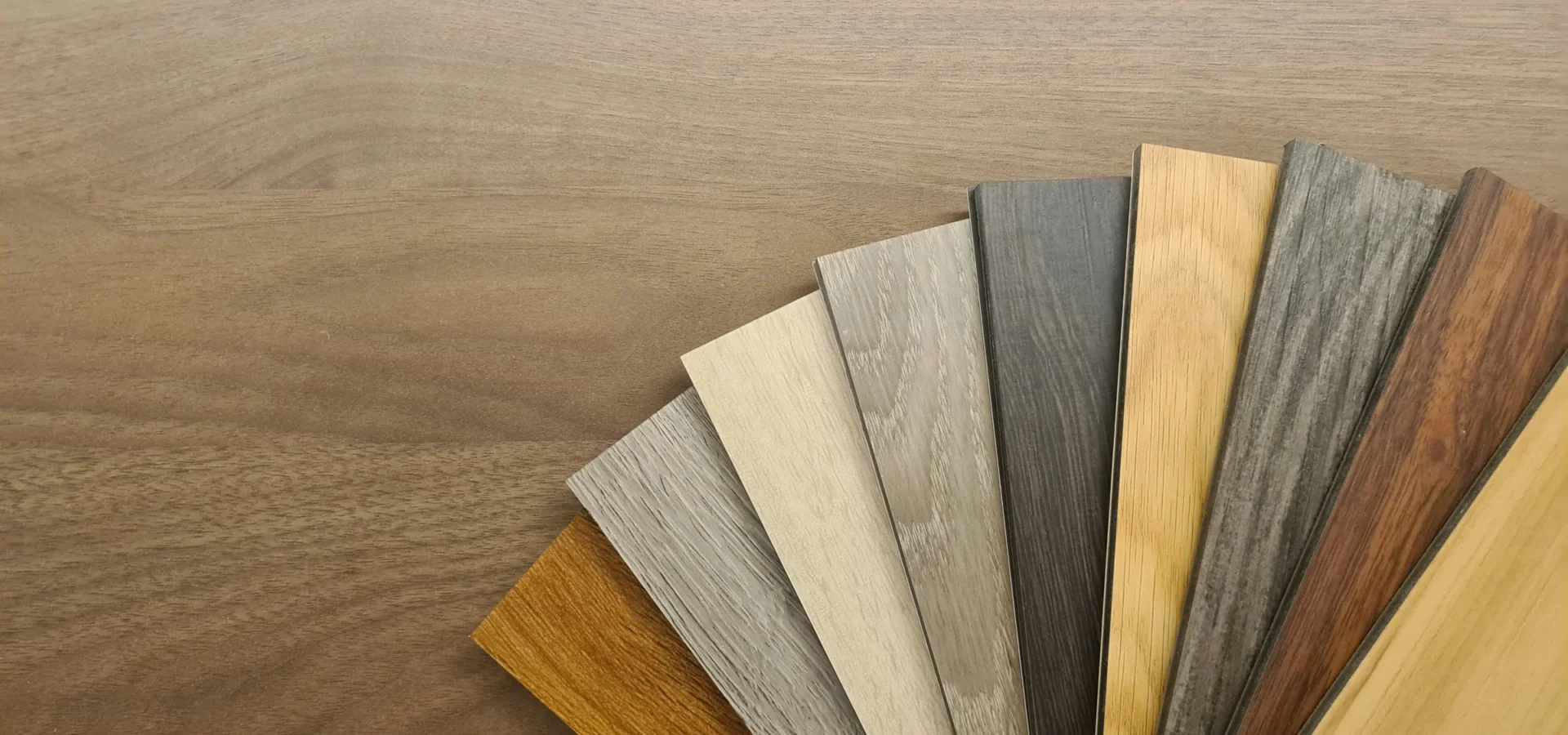 Wood flooring samples in various finishes displayed in a fan arrangement on a wooden surface.