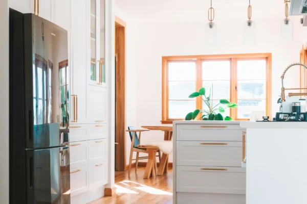 Modern kitchen with white cabinetry, wood-trimmed windows, wooden island, copper pendant lights, and ocean view in background.