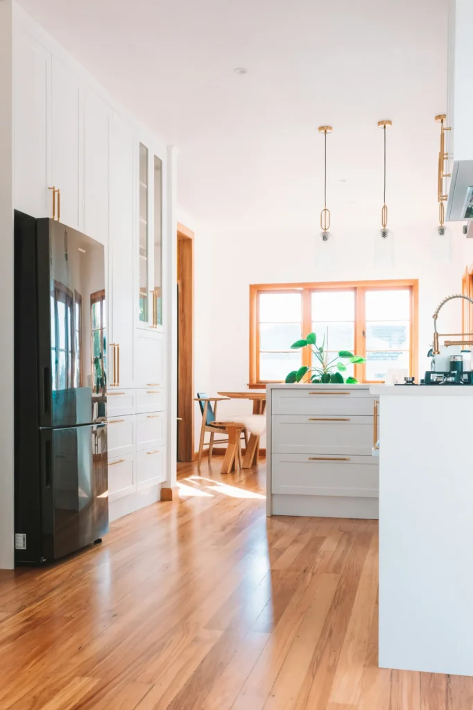 Modern kitchen with white cabinetry, wood-trimmed windows, wooden island, copper pendant lights, and ocean view in background.