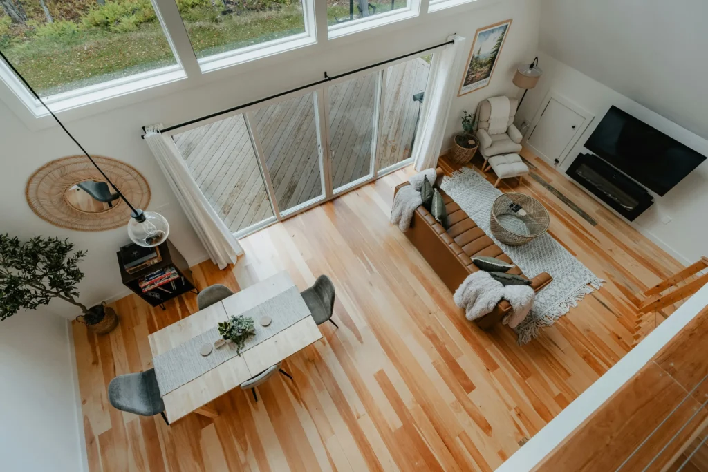 Overhead view of a bright loft living room with hardwood floors, modern furniture, large windows, and natural decor elements.