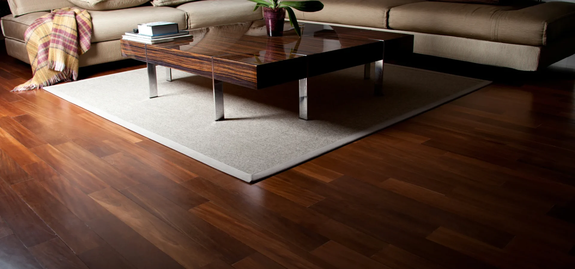 Modern living room with beige sectional sofa, dark wood coffee table, potted orchid, and polished hardwood flooring.