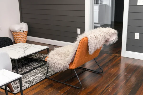 Modern living room with orange leather chair draped in white fur, marble coffee table, and dark shiplap accent wall.